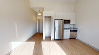 Located at 2130 S Michigan Ave in Chicago's vibrant South Loop neighborhood, this single-floor studio unit offers a clean, modern design with an efficient and well-planned layout. The open main living area features light-toned hardwood-style flooring and tall ceilings that lend an airy sense of space, with natural light streaming in through large double windows offering views of the surrounding cityscape.

The kitchen is neatly integrated into the living space and is outfitted with white cabinetry, stainless steel appliances including a full-size refrigerator, microwave, dishwasher, and a sink — providing full functionality in a compact footprint. A dedicated closet with built-in shelving offers practical storage directly within the main area.

The bathroom is clean and straightforward, featuring a full bathtub and shower combination, a vanity with sink, and a toilet, all finished in neutral tones with hardwood-style flooring carried throughout. Additional utility features, including an electrical panel, are conveniently recessed into the wall. The unit's neutral color palette, modern finishes, and abundant natural light create a bright and inviting atmosphere suited for comfortable urban living.