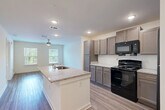 Located at 1928 Waycrest Dr SW in Atlanta, GA, this single-story 1-bedroom, 1-bathroom residence offers a thoughtfully designed layout with modern finishes throughout. The open-concept kitchen and living area serves as the heart of the home, anchored by a central island with a granite countertop and built-in sink. The kitchen is equipped with gray shaker-style cabinetry, granite countertops, black appliances including a range, microwave, and refrigerator, and recessed lighting overhead. The living area extends naturally from the kitchen, bathed in natural light from dual windows and cooled by a ceiling fan. Wood-look plank flooring runs consistently throughout the entire space, lending warmth and cohesion. The bedroom is a comfortable, well-lit retreat featuring a ceiling fan, a large window with views of lush greenery, and access to two generously sized closets outfitted with multi-tier wire shelving systems. The bathroom is clean and contemporary, showcasing a walk-in tiled shower, a granite-topped vanity with gray cabinetry, and wood-look flooring. Additional functional spaces include a dedicated laundry area and a utility room, rounding out this efficiently organized and move-in-ready home.