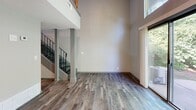 This two-story residence is thoughtfully organized across two levels, with the lower floor housing the main living areas and the upper floor dedicated to private quarters. The layout offers a well-defined separation between communal and personal spaces.

The ground floor makes an immediate impression with its dramatic double-height living room, where soaring ceilings amplify the sense of openness. Large sliding glass doors flood the space with natural light and provide direct views of surrounding greenery. A staircase with sleek metal railings anchors the room and connects the two levels. The kitchen features gray cabinetry, granite-style countertops, stainless steel appliances, and a textured stone tile backsplash, offering both functionality and visual interest. Light hardwood-style flooring runs throughout the lower level.

Upstairs, the primary bedroom is a comfortable, well-proportioned retreat with its own window allowing natural light and outdoor views. The upper level also includes two closets, providing ample storage. The full bathroom features a tiled tub-shower combination with chrome fixtures in a clean, neutral palette. A hallway with overhead lighting and light wood-style flooring connects the upper-floor rooms, completing a practical and cohesive layout.