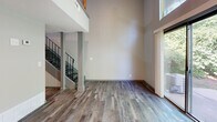 This two-story residence is thoughtfully organized across two levels, with the lower floor housing the main living areas and the upper floor dedicated to private quarters. The layout offers a well-defined separation between communal and personal spaces.

The ground floor makes an immediate impression with its dramatic double-height living room, where soaring ceilings amplify the sense of openness. Large sliding glass doors flood the space with natural light and provide direct views of surrounding greenery. A staircase with sleek metal railings anchors the room and connects the two levels. The kitchen features gray cabinetry, granite-style countertops, stainless steel appliances, and a textured stone tile backsplash, offering both functionality and visual interest. Light hardwood-style flooring runs throughout the lower level.

Upstairs, the primary bedroom is a comfortable, well-proportioned retreat with its own window allowing natural light and outdoor views. The upper level also includes two closets, providing ample storage. The full bathroom features a tiled tub-shower combination with chrome fixtures in a clean, neutral palette. A hallway with overhead lighting and light wood-style flooring connects the upper-floor rooms, completing a practical and cohesive layout.