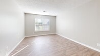 Located at 3309 River Chase Court in Louisville, KY, this single-floor home offers a practical and comfortable layout across three bedrooms, a living room, kitchen, and hallway. The kitchen is a standout feature, showcasing granite countertops, crisp white cabinetry with modern hardware, and a full suite of stainless steel appliances including a dishwasher, range, and refrigerator. Natural light filters in through a window, brightening the space and highlighting the warm hardwood-style flooring that extends throughout the kitchen and main living areas. The living room is a bright, open space with the same light flooring and neutral gray walls, creating a clean and versatile canvas. The three bedrooms feature plush carpeting and neutral tones, each with windows that bring in natural light and views of the surrounding greenery. The spacious primary bedroom is particularly notable, offering dual bi-fold closets for generous storage. The additional bedrooms are well-proportioned, each with a closet and window. Textured ceilings and clean white trim are consistent throughout, contributing to a cohesive and tidy aesthetic across the entire home.