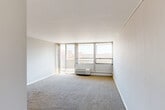 Located at 2200 Fuller Rd in Ann Arbor, Michigan, this one-bedroom, one-bathroom unit offers a well-organized layout across a single floor. The combined living and dining area is bright and open, featuring large floor-to-ceiling windows that flood the space with natural light and offer expansive views of the surrounding cityscape. Carpeted flooring adds warmth to the living spaces, while tile flooring transitions into the entryway and kitchen. A sliding glass door leads to a private balcony, extending the living space outdoors. The kitchen has been thoughtfully updated with two-tone cabinetry in grey and blue, white quartz countertops, a subway tile backsplash, stainless steel appliances including a refrigerator, range, and microwave, and a central island with additional counter space. Track lighting overhead provides excellent task illumination. A pantry offers convenient additional storage. The bedroom is a comfortable size, featuring carpet, a large window with city views, and a wall-mounted HVAC unit. Two closets provide ample storage throughout the unit. The bathroom is finished with classic white subway tile surrounding a full bathtub and shower, complemented by a white vanity and mirrored medicine cabinet.