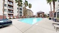 Located at 3111 S St in Sacramento's vibrant 95816 neighborhood, this outdoor amenity space centers around a generously sized, resort-style swimming pool with crystal-clear turquoise water. The pool deck is finished in smooth concrete and lined with multiple lounge chairs and chaise seating, providing ample space for sunbathing and relaxation. Towering palm trees are strategically placed throughout the courtyard, adding a tropical aesthetic and natural shade.

A standout architectural feature is the brick-constructed pavilion with a metal hip roof, which serves as a covered outdoor gathering area. Adjacent to the pavilion is an outdoor kitchen area equipped with what appears to be a pizza oven and grilling stations, making it ideal for social gatherings. Comfortable sectional seating is arranged nearby for additional lounging.

The pool area is enclosed by decorative iron fencing with brick accent walls, accented by manicured shrubs and blue decorative gravel landscaping. The surrounding multi-story building features balconies that overlook the courtyard, offering residents elevated views of the pool and green spaces below. Wall-mounted lantern-style lighting and blue fabric awnings on the building facade add architectural charm. The overall ambiance is welcoming, well-maintained, and designed for outdoor leisure and community enjoyment.