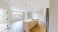 This well-appointed 2-bedroom, 2-bathroom single-floor residence at 2460–2480 Main St in Rocky Hill, CT offers a thoughtfully designed open-concept layout. The combined kitchen and living area serves as the heart of the home, highlighted by a large center island with a light wood finish, white quartz countertops, and an undermount sink. Stainless steel appliances, white upper cabinetry, and a row of elegant brass pendant lights complete the modern kitchen aesthetic. Warm hardwood-style flooring flows throughout the main living areas, while abundant natural light pours in through large windows that frame outdoor views. A ceiling fan in the living room adds comfort to the airy space. The primary bedroom features plush carpeting, a walk-in closet with wire shelving, and a private en-suite bathroom outfitted with wood-tone vanity cabinetry, a white quartz countertop, and hardwood-style flooring. Each bedroom offers ample closet storage. A dedicated in-unit laundry room houses a full-size washer and dryer. Neutral warm-toned walls, clean white trim, and black door hardware provide a cohesive, contemporary feel throughout this move-in-ready residence.