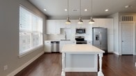 Located on Swiss Avenue in Dallas's vibrant 75204 zip code, this single-story residence combines modern design with functional living. The kitchen serves as a standout feature, showcasing crisp white shaker cabinetry, a classic subway tile backsplash, and a suite of stainless steel appliances including a range, microwave, dishwasher, and French door refrigerator. A central island with elegant turned legs and pendant lighting overhead provides additional prep space and a casual gathering spot. Rich dark hardwood flooring runs throughout the main living areas, adding warmth and contrast to the bright, neutral palette. Windows along the kitchen wall invite natural light and offer views of the surrounding neighborhood. The bathroom is thoughtfully appointed with a white vanity offering generous drawer storage, a framed mirror with wall sconce lighting, a quartz countertop, and a full tub-shower combination accented by neutral stone-look tile. The bedroom features soft wall-to-wall carpeting, muted gray tones, and a closet, offering a comfortable and restful retreat. Throughout the space, clean lines, brushed nickel hardware, and a cohesive neutral color scheme create a polished, move-in-ready atmosphere suited to modern urban living.