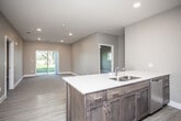 This single-floor residence offers a well-designed open-concept layout that seamlessly connects the kitchen and living areas. The kitchen is a standout feature, equipped with dark wood cabinetry, stainless steel appliances including a refrigerator, microwave, and range, and a large island with a white countertop and undermount sink. Light wood-style flooring runs throughout the kitchen and entry areas, transitioning to plush carpet in the living and bedroom spaces.

The spacious living area benefits from recessed lighting and a sliding glass door that opens to an outdoor view of lush greenery, filling the space with natural light. A secondary window in an adjacent room further enhances the connection to the outdoors.

The bedrooms are generously sized, each featuring soft carpeting and walk-in closets with built-in shelving. The bathroom is thoughtfully appointed with a dark wood vanity, white countertop, a tub and shower combination, light wood-style flooring, and a grab bar for added accessibility. A walk-in closet accessible from the bathroom adds convenient storage. The overall palette of warm neutrals and natural tones creates a clean, modern, and welcoming ambiance throughout.