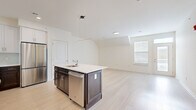 This single-floor residence showcases a thoughtfully designed open-concept layout unified by light hardwood flooring throughout. The kitchen serves as a central highlight, featuring a two-tone design with crisp white upper cabinetry and dark lower cabinets, complemented by a light-colored tile backsplash. A center island with a white countertop provides an integrated sink, dishwasher, and pendant lighting overhead. Stainless steel appliances, including a gas range, built-in microwave, and refrigerator, complete the well-appointed kitchen.

The open living area extends from the kitchen, offering generous space with vaulted ceiling sections that add architectural character. Natural light enters through multiple windows fitted with blinds, and a glass-panel door leads to an outdoor balcony, enhancing the connection to the exterior. Additional rooms feature the same vaulted ceiling detail and neutral white walls, providing versatile, light-filled spaces. The bathroom includes a soaking tub with a tiled surround in a warm stone-like finish, a coordinating tile floor, and chrome fixtures, delivering a clean and contemporary aesthetic throughout.