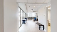 Located on Chestnut Street in the heart of Philadelphia's Center City, this compact yet well-appointed lounge space offers a thoughtfully designed single-floor layout comprising a living room, hallway, and bathroom. The living area is the centerpiece of the space, bathed in natural light through expansive floor-to-ceiling glass doors and windows that frame sweeping views of the Philadelphia skyline. Light wood-style flooring and a suspended tile ceiling lend a clean, contemporary aesthetic throughout. The lounge area features a curved gray sectional sofa accented with vivid blue throw pillows, a round marble-top coffee table, a decorative geometric mirror, and a wall-mounted flat-screen television — creating a comfortable and stylish gathering area. A bar-height counter along one window wall, lined with modern neutral-toned stools, provides an additional seating option alongside small bistro tables and navy accent chairs. A smart vending unit offers convenient refreshment access. The glass doors open to an outdoor terrace with additional seating, extending the usable space and providing an open-air retreat with panoramic city views. The ADA-accessible bathroom is finished with light tile flooring, granite-accented countertops, and stainless steel grab bars, ensuring accessibility and functionality. This space is ideal for use as a communal lounge or amenity area.