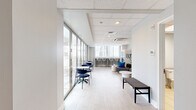 Located on Chestnut Street in the heart of Philadelphia's Center City, this compact yet well-appointed lounge space offers a thoughtfully designed single-floor layout comprising a living room, hallway, and bathroom. The living area is the centerpiece of the space, bathed in natural light through expansive floor-to-ceiling glass doors and windows that frame sweeping views of the Philadelphia skyline. Light wood-style flooring and a suspended tile ceiling lend a clean, contemporary aesthetic throughout. The lounge area features a curved gray sectional sofa accented with vivid blue throw pillows, a round marble-top coffee table, a decorative geometric mirror, and a wall-mounted flat-screen television — creating a comfortable and stylish gathering area. A bar-height counter along one window wall, lined with modern neutral-toned stools, provides an additional seating option alongside small bistro tables and navy accent chairs. A smart vending unit offers convenient refreshment access. The glass doors open to an outdoor terrace with additional seating, extending the usable space and providing an open-air retreat with panoramic city views. The ADA-accessible bathroom is finished with light tile flooring, granite-accented countertops, and stainless steel grab bars, ensuring accessibility and functionality. This space is ideal for use as a communal lounge or amenity area.