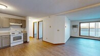 Located at 9900 Redwood St NW in Coon Rapids, Minnesota, this two-bedroom, one-bathroom unit offers a functional and well-organized single-floor layout. The combined kitchen and living area serves as the heart of the home, featuring light wood-tone flooring, a textured ceiling, and a wall-mounted air conditioning unit. The kitchen is outfitted with taupe cabinetry, light countertops, a double-basin sink, and white appliances including a refrigerator, dishwasher, and electric range. A sliding glass door in the living area provides access to an outdoor balcony and brings in natural light with views of the surrounding landscape. Both bedrooms are carpeted and feature wood-trimmed windows with vertical blinds and baseboard heating. The primary bedroom includes a ceiling fan with light fixture. Four closets throughout the unit offer generous storage. The full bathroom is finished with wood-tone flooring, a single-sink vanity with storage cabinetry, a wall-mounted light fixture above a framed mirror, and a tub/shower combination. Baseboard heating is present throughout, and the textured ceilings are consistent across the unit, contributing to a cohesive, clean aesthetic.
