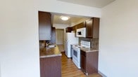 This multi-floor space spans three levels, offering a thoughtfully laid-out interior designed for practical everyday living. The kitchen is a standout feature, showcasing rich dark wood cabinetry that provides ample storage both above and below the countertops. The granite-style countertops add a touch of warmth and durability, complementing the deep tones of the cabinetry. White appliances — including a refrigerator, electric range, and over-the-range microwave — are neatly integrated into the kitchen layout, creating a clean and cohesive look. A double-basin sink is positioned along the counter, offering convenience for meal preparation and cleanup. The kitchen backsplash features a neutral stone-like tile that ties the design elements together seamlessly. Light wood-tone flooring runs through the kitchen and into the adjoining hallway, lending a warm and inviting feel to the space. The open pass-through design of the kitchen connects it naturally to the rest of the living areas, promoting an easy flow between spaces. Flush-mount ceiling lighting provides consistent illumination throughout. With its practical layout and durable finishes, this space is well-suited for comfortable, day-to-day living across all three floors.