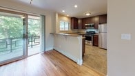 This upgraded single-floor residence offers two bedrooms and one bathroom within a well-planned layout. The living area features light hardwood flooring that extends toward a sliding glass door, opening to a private balcony with outdoor views of mature trees. A ceiling fan overhead and a large picture window allow ample natural light to fill the space, creating a bright and open atmosphere.

The kitchen is thoughtfully designed with rich dark-wood cabinetry, granite countertops, and a breakfast bar peninsula that provides additional seating and workspace. Stainless steel appliances—including a gas range, microwave, refrigerator, and dishwasher—complement the tile flooring and recessed lighting, delivering both style and functionality.

Both bedrooms are carpeted and feature neutral wall tones, baseboard heating, and windows with views of surrounding greenery. The primary bedroom benefits from dual windows and a ceiling fan, enhancing comfort and ventilation.

The bathroom has been fully upgraded, showcasing tile flooring, a walk-in shower with glass doors and large-format tile surround, a dark-wood vanity with granite countertop, and a wall-mounted storage cabinet, providing a clean, modern aesthetic throughout.