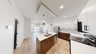 This well-appointed single-story unit offers a thoughtfully organized layout encompassing a combined kitchen and living area, one bedroom, one full bathroom, and a dedicated laundry room. Wood-look porcelain tile flooring flows consistently throughout, lending warmth and visual continuity across the entire space.

The open kitchen is a standout feature, showcasing a two-tone design with rich walnut-finish lower cabinets paired with crisp white upper cabinetry and matte black hardware. A marble-look tile backsplash adds elegance, while a peninsula with a white quartz countertop and undermount sink provides additional workspace and seating. Stainless steel appliances and a pendant light complete the modern aesthetic.

The living area is bright and airy, with recessed lighting, a ceiling fan, and sliding glass doors that open to a private balcony with outdoor views. Bold black interior doors provide a striking contrast against the white walls throughout.

The bathroom features wood-toned cabinetry, a tub-shower combination with marble-look tile surround, a frameless sliding glass enclosure, and matte black fixtures. The bedroom is a comfortable, well-lit retreat with a ceiling fan and recessed lighting. A separate laundry room accommodates a full-size washer and dryer with overhead shelving.