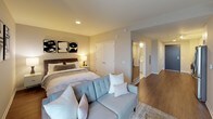 This single-floor unit showcases a thoughtfully designed layout that balances functionality and modern style. The kitchen is a standout feature, outfitted with stainless steel appliances including a gas range, dishwasher, microwave, and refrigerator. Crisp white cabinetry extends to the ceiling, complemented by a white subway tile backsplash, dark countertops, and warm hardwood-style flooring. Track lighting overhead ensures the space is well-illuminated. A bold navy entry door adds a striking design accent at the unit's entrance.

The living area is anchored by a large window offering elevated city views, flooding the space with natural light. A wall-mounted media console and decorative wall art contribute to the room's contemporary character. The bedroom is generously proportioned, featuring recessed lighting, hardwood-style flooring, and a large window framing additional urban views, creating a bright and restful retreat.

The bathroom is designed with accessibility in mind, featuring grab bars, a walk-in shower with subway tile surround and curtain, light tile flooring, and a clean white vanity with ample storage. Neutral tones and consistent finishes throughout the unit create a cohesive, polished aesthetic.