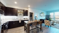 This single-floor residence is designed with a modern aesthetic and functional open-concept layout. The kitchen serves as a central focal point, featuring dark espresso cabinetry with sleek bar-pull hardware, white quartz countertops, stainless steel appliances including a refrigerator, electric range, and built-in microwave, and under-cabinet lighting. Open glass shelving adds a contemporary touch, while a freestanding kitchen island with lower storage and bar seating provides additional prep space and casual dining.

The kitchen flows seamlessly into the living area, which benefits from natural light through large windows fitted with horizontal blinds. Light wood-style flooring runs throughout the main living spaces, contributing to a clean, cohesive look.

In-unit laundry with a stacked washer and dryer is conveniently located between the kitchen and bedroom, maximizing accessibility without sacrificing space.

The bedroom is carpeted and comfortably sized, featuring a large window with outdoor views and ample wall space. The bathroom is finished consistently with the rest of the unit, showcasing dark cabinetry, a white countertop vanity, a large mirror, and light wood-style flooring. Recessed lighting throughout the unit ensures well-distributed illumination in every room.