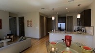 This single-floor residence offers a thoughtfully designed open-concept layout that seamlessly connects the living, dining, and kitchen areas into one cohesive and functional space. The interior is finished with light hardwood flooring that extends throughout, lending warmth and continuity to the overall design.

The kitchen serves as a central focal point, featuring dark cabinetry, granite countertops, and stainless steel appliances, including a French door refrigerator. A peninsula with a built-in sink provides additional workspace and casual seating, while a pendant light above adds a refined touch.

Adjacent to the kitchen, the dining area accommodates a round glass-top table with modern wire-frame chairs, creating an intimate setting ideal for meals and gatherings. The living area is defined by a contemporary sofa and accented by colorful wall art, adding personality to the neutral palette of the space.

Multiple interior doors lead to additional rooms, suggesting a well-organized floor plan with distinct private spaces. Recessed lighting throughout ensures even, ambient illumination, complementing the clean lines and modern finishes that define this residence's aesthetic. The overall atmosphere is contemporary, comfortable, and move-in ready.