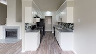 This two-floor space offers a clean, contemporary aesthetic with a neutral gray color palette and wood-look flooring that runs consistently throughout. The open living area is bright and airy, featuring a ceiling fan, white-trimmed windows with blinds, and a welcoming entry door that allows natural light to flow in. The galley-style kitchen is well-equipped, showcasing white cabinetry on both sides, gray granite-style countertops, a mosaic tile backsplash with black and green accents, black appliances including a range and refrigerator, and a stainless steel sink. Ample upper and lower cabinet storage makes the kitchen both functional and visually appealing. The bedrooms are comfortably sized, each featuring ceiling fans, windows with blinds for natural light, and sliding or hinged closets with built-in shelving for storage. The bathrooms are finished with gray granite-style vanity countertops, white cabinetry, framed mirrors, and a full tub-shower combination. Textured walls and clean white trim add a subtle depth throughout the bathrooms. Overall, the space maintains a consistent, modern finish with practical layouts designed for comfortable everyday living across both floors.