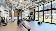 Located at 1720 Research Park Dr in Davis, CA, this fitness center offers a generously sized, single-floor exercise space designed with both functionality and aesthetics in mind. The industrial-modern interior features soaring ceilings with exposed ductwork and linear LED lighting, creating a bright and energizing atmosphere throughout.

The cardio zone is anchored by multiple treadmills and an elliptical machine, all positioned to take advantage of expansive floor-to-ceiling windows that flood the space with natural light and provide views of the surrounding outdoor greenery. Wall-mounted flat-screen TVs are stationed throughout for entertainment during workouts.

The strength training area is well-appointed with a multi-functional cable machine, weight bench, and a smith machine with integrated weight storage. A dedicated functional training zone features suspension trainers, kettlebells, medicine balls, stability balls, and plyo boxes neatly organized on a storage rack. Full-length mirrors along one wall, accented by warm wood slat paneling, enhance the sense of space and support form checking.

The flooring throughout is a durable, neutral-toned gym surface suited for high-traffic use. Additional amenities include a built-in dual-level water fountain station and a ceiling fan for supplemental air circulation, ensuring a comfortable and practical environment for all fitness levels.