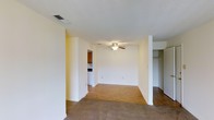 Located at 203 N Cleveland Ave in Long Beach, Mississippi, this single-story property offers a straightforward and functional layout designed for comfortable everyday living. The main living area is open and airy, featuring a combination of hardwood-style flooring and plush carpeting that delineates different zones within the space. A ceiling fan with a light fixture is centrally mounted, providing both air circulation and ambient lighting throughout the room. The light-toned walls contribute to a bright and clean atmosphere, while the textured ceiling adds a subtle architectural detail. A conveniently placed closet with a rod for hanging storage is accessible directly from the living area, adding practical organization space. The kitchen is visible from the main living space and is outfitted with wooden cabinetry and standard appliances, maintaining a cohesive and utilitarian design. HVAC vents integrated into the ceiling ensure year-round climate comfort. The overall layout of this single-floor property is efficient and well-connected, making it easy to navigate between the living, kitchen, and storage areas. The neutral color palette and simple finishes create a versatile backdrop suitable for a variety of interior styles and furnishings.
