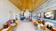Located at 6741 Boulder Hwy in Las Vegas, Nevada, this single-floor community clubhouse at PARQ offers a generously sized, thoughtfully designed gathering space that blends vibrant contemporary style with practical amenities. The centerpiece of the space is a dramatic vaulted wood-paneled ceiling that rises to impressive heights, anchored by a striking sculptural gold chandelier that adds warmth and elegance throughout. Light-toned wide-plank flooring runs throughout, complementing the airy, open layout.

The main lounge area features a curved navy sectional sofa, richly upholstered leather accent chairs in cognac tones, and layered area rugs, all arranged around a modern fireplace set into a textured tile feature wall. A large-scale abstract wallcovering in cool grey tones serves as a dramatic backdrop for curated framed artwork illuminated by brass picture lights.

A dedicated entertainment zone branded "PARQ" showcases arcade gaming stations, marble-topped café tables, and navy dining chairs — perfect for social gatherings. Floor-to-ceiling windows flood a secondary lounge with abundant natural light and views of the outdoor amenity courtyard. A built-in shelving display and a cozy nook with hexagonal plant wall installation add character and greenery to the space, creating a welcoming, resort-inspired community atmosphere.