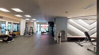 Located at 8809 Washington Blvd in Culver City, CA, this contemporary fitness center offers a well-appointed, single-floor layout designed to support a full range of workout styles. The main exercise area is generously proportioned, featuring rubber flooring throughout for durability and safety. Recessed square skylights and flush ceiling panels provide even, bright illumination across the space, creating an energizing atmosphere.

The cardio zone is equipped with multiple treadmills and an elliptical trainer, positioned in front of large wall-mounted mirrors and warm wood-accented mirror frames that visually expand the room. A dumbbell rack with a full range of weights occupies a dedicated corner, complementing the cardio offerings. A separate functional training area houses TRX suspension trainers, medicine balls, a rowing machine, and a stationary bike, giving members diverse training options.

A flexible, open-plan studio room with soft green accent walls and carpeted floors connects to the main gym via glass-panel folding doors, making it ideal for group classes or stretching. The entry corridor features bold chevron-patterned wall art, glass-walled partitions, and a hydration station, contributing to the polished, modern aesthetic. Natural light filters in through street-facing windows, adding a welcoming brightness to the overall environment.