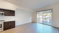 Located at 1640 East Plaza Boulevard in National City, CA, this well-appointed one-bedroom, one-bathroom residence offers a clean, modern aesthetic throughout its thoughtfully designed single-floor layout. Light wood-tone flooring runs continuously through the living spaces, creating a warm and cohesive feel.

The open-concept living, dining, and kitchen area forms the heart of the unit. The kitchen is outfitted with rich dark-stained cabinetry, white countertops, and a full suite of stainless steel appliances including a refrigerator, range, built-in microwave, and dishwasher. Recessed lighting adds a polished finish. The living area benefits from abundant natural light, with large sliding glass doors opening onto a private balcony that overlooks lush outdoor greenery.

The spacious bedroom features multiple windows that invite generous sunlight, complemented by a dedicated closet and an in-unit laundry area for added convenience. The bathroom is clean and modern, featuring a tub-shower combination, a wall-mounted vanity with white countertop, and wood-look flooring that ties seamlessly to the rest of the unit.

Crisp white walls throughout the unit enhance the bright, airy ambiance, while the efficient hallway layout ensures smooth flow between all rooms. This residence combines practical functionality with contemporary design in a compact yet comfortable footprint.