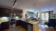 The Berkley's 2-bedroom, 2-bathroom floor plan in Spring, TX is a single-story residence designed with a cohesive, modern aesthetic. The open-concept kitchen serves as a central hub, featuring dark espresso cabinetry, granite countertops, a tile backsplash, stainless steel appliances, and a peninsula island with pendant lighting overhead. Track lighting illuminates the kitchen, which flows directly into a spacious living area finished with wood-style flooring. The living room offers generous natural light through large windows and French doors, which also provide outdoor access, and is topped with a ceiling fan. A dark accent wall adds depth and contrast to the space.

Both bedrooms are carpeted and include ceiling fans. The primary bedroom features a bold dark accent wall, while the secondary bedroom offers bright natural light from multiple windows. Each bathroom is outfitted with dark-framed vanity mirrors, granite-topped dark cabinetry, and undermount sinks. The primary bath includes a soaking tub with a shower curtain surround. A hallway connects the secondary bath to its adjacent bedroom, with hardwood-style flooring carrying throughout the corridor. The overall design is contemporary, cohesive, and richly detailed.