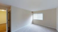 This single-floor space presents a clean and understated aesthetic, designed with simplicity and functionality in mind. The interior is finished in soft, neutral beige tones on the walls and ceiling, creating a warm and inviting atmosphere that feels open and easy to personalize.

The room is carpeted in a light, plush material that adds comfort underfoot and contributes to the overall sense of calm throughout the space. White baseboards run along the perimeter of the room, providing a crisp contrast to the warm wall tones and adding a polished, finished look to the interior.

A centrally positioned window fitted with horizontal blinds allows for adjustable natural light, filling the room with a soft, diffused glow. The window offers an outward view and contributes to a sense of airiness, making the space feel bright without being overwhelming. The smooth, white ceiling complements the neutral palette and helps reflect light throughout the room.

The layout is open and uncluttered, offering flexibility for a variety of uses. Wall outlets are thoughtfully placed, adding to the practical, livable nature of the space. Overall, this single-floor property combines a clean design with comfortable finishes, making it a welcoming and versatile environment.