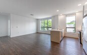 This single-floor unit showcases a clean, contemporary design characterized by crisp white walls, rich hardwood flooring, and an abundance of natural light. The entry opens into a bright, open-concept living and kitchen area where large windows frame views of the surrounding neighborhood's rooftops and greenery. The kitchen is well-appointed with light wood cabinetry, quartz countertops, stainless steel appliances including a gas range and over-the-range microwave, and a peninsula that provides additional workspace and defines the living area. Recessed lighting complements the natural light throughout.

The living space flows toward multiple bedrooms, each featuring hardwood floors, white walls, and generously sized windows fitted with blinds. At least one bedroom includes a dedicated walk-in closet with built-in shelving. The unit is served by two bathrooms: one features hexagonal gray floor tile, a glass-enclosed walk-in shower with white subway tile, and wood-accented cabinetry, while the second includes a full tub-shower combination with white tile surround. The entry foyer is compact and functional, completing the unit's thoughtfully organized layout.