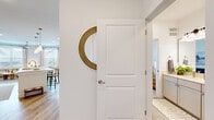 This well-designed 2-bedroom, 1-bathroom residence spans a single floor and features a clean, modern aesthetic with warm neutral tones and quality finishes throughout. The entry hall welcomes visitors with crisp white walls and a decorative round mirror, offering glimpses into both the kitchen and living areas.

The kitchen is a functional galley-style space equipped with stainless steel appliances, two-tone cabinetry in warm wood and soft white, light quartz countertops, a subway tile backsplash, and warm hardwood-style flooring. Pendant lighting adds a refined touch above the counter.

The living room is bright and inviting, featuring large windows dressed with linen curtains that allow abundant natural light and outdoor views of the surrounding neighborhood. Hardwood-style flooring continues here, complementing the comfortable, welcoming atmosphere.

Both bedrooms are carpeted and well-lit, with large windows, ceiling fans, and a serene, restful ambiance. The primary bedroom offers a generous footprint with access to natural light and a spacious closet.

The bathroom is elegantly finished with large-format tile flooring, a white subway-tiled tub and shower combination with a curved curtain rod, and a wide vanity with ample cabinetry. A second bathroom area features an extended vanity with a single sink and generous storage, maintaining the home's cohesive, polished style.