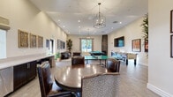 Located at 2615 E Date Palm Street in Ontario, CA, this single-floor game room is a well-appointed recreational space designed for both entertainment and relaxed social gatherings. The room features soaring ceilings with recessed lighting and elegant chandelier pendant fixtures that cast a warm, inviting glow throughout the space. Wood-look tile flooring runs across the entire room, adding a clean, contemporary aesthetic that complements the neutral warm-toned walls.

The game area is thoroughly equipped, featuring a full-size pool table with a bold blue finish, a regulation ping pong table, and a foosball table, offering a variety of entertainment options. A large wall-mounted flat-screen TV is positioned prominently on one wall, ideal for watching sports or gaming. A dedicated lounge area provides comfortable leather seating arranged around a herringbone-patterned wood coffee table, accompanied by framed artwork that adds a refined touch.

Additional highlights include a built-in wet bar with dark cabinetry and light countertops, a round dining table with upholstered chairs for casual seating, and tall windows and glass French doors that allow natural light to filter in while offering views of the outdoor surroundings. Lush indoor plants are thoughtfully placed throughout, enhancing the room's inviting and lively atmosphere.