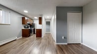 This single-floor residence offers a practical and cohesive layout designed for comfortable everyday living. The open-concept living and kitchen area serves as the heart of the home, where rich wood-look vinyl plank flooring extends seamlessly underfoot. A wall-mounted air conditioning unit and baseboard heating provide year-round climate control, while a wide window brings in natural light and views of the surrounding area.

The galley-style kitchen is efficiently designed with warm, rich-toned wood cabinetry lining both sides, light granite-look countertops, and a full suite of stainless steel appliances including a range, refrigerator, and dishwasher. Recessed lighting above keeps the space well-lit and functional.

A hallway connects the main living area to the private spaces, including bedrooms finished with plush neutral carpeting. One bedroom features a mirrored sliding-door closet, adding a sense of depth to the room. The bathroom is finished with a wide wood vanity topped with a light granite-style countertop, an undermount sink, and brushed nickel fixtures, giving it a clean and refined look. Textured ceilings throughout add a classic character to the overall design of this move-in-ready home.