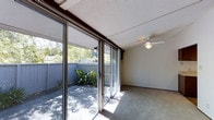 This single-floor space offers a seamless connection between indoor and outdoor living. The main living area is defined by a wall of sliding glass doors that flood the interior with natural light and provide direct access to a private enclosed patio. The patio is bordered by a wood fence and features mature greenery and plantings, creating a tranquil outdoor retreat with excellent privacy.

Inside, the living area is finished with wall-to-wall carpet and neutral-toned walls, giving the space a clean and versatile aesthetic. A ceiling fan with a built-in light fixture is centrally mounted, providing both air circulation and ambient lighting. The textured ceiling adds a subtle architectural detail throughout the room.

The abundance of natural light streaming through the full-length glass doors creates a bright and airy atmosphere, while the outdoor views of trees and foliage enhance the sense of connection to the natural surroundings. The layout is open and functional, lending itself well to a variety of furnishing arrangements. Overall, the space balances practical interior features with an inviting indoor-outdoor flow, making it well-suited for comfortable everyday living.
