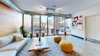 Located at 1924 8th St NW in Washington, DC's vibrant Shaw neighborhood, this single-floor space offers a thoughtfully designed open-plan layout that balances industrial aesthetics with warm, inviting elements. Polished concrete floors run throughout, providing a sleek, durable foundation that ties the entire space together.

The living area is a standout, anchored by a full-wall warm wood accent feature that adds natural texture and richness to the interior. Exposed metallic ductwork runs overhead, reinforcing the industrial character of the space, while track lighting ensures flexible, well-distributed illumination. A comfortable sectional sofa, live-edge wood coffee table, and vibrant yellow ottomans create a welcoming and contemporary seating arrangement.

Floor-to-ceiling glass sliding doors flood the interior with abundant natural light and open directly onto an outdoor terrace furnished with seating — a seamless indoor-outdoor connection ideal for relaxing or entertaining. The opposing end of the space features a bar-height counter with seating, backed by a decorative patterned tile wall and pendant lighting, alongside curated artwork displayed on crisp white walls. Lush potted plants are positioned throughout, softening the industrial elements and adding life to the overall ambiance.