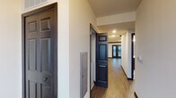 This single-floor space presents a cohesive and modern interior defined by rich dark wood trim, dark-paneled doors, and durable hardwood-style flooring that flows throughout the main living areas. A welcoming hallway with recessed lighting connects the various rooms, creating a logical and accessible layout.

The main living area is expansive and filled with natural light, featuring a striking set of dark-framed French doors that open outward and are flanked by windows fitted with horizontal blinds. Bold crown molding in dark tones frames the room, adding a polished architectural detail.

The kitchen is well-equipped and efficient, showcasing dark espresso cabinetry with ample storage, granite-look countertops, and a full suite of stainless steel appliances including a refrigerator, electric range, over-the-range microwave, and dishwasher. Recessed lighting illuminates the workspace effectively.

The bedroom offers a calm and comfortable retreat, carpeted for warmth and featuring a large window that invites natural light. An additional open room with hardwood-style floors and dark crown molding provides flexible use as a dining or office space.

The bathroom is thoughtfully finished with a classic black-and-white mosaic tile floor, dark vanity cabinetry, a white countertop with dual sinks, a large mirror, and a full-size shower-tub combination with brushed nickel fixtures.