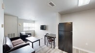 Located at 2900 River Dr in Moline, IL, this single-floor, one-bedroom, one-bathroom unit offers a well-organized and efficient layout across a compact yet functional footprint. Light wood-style flooring flows throughout, complementing the clean, neutral-toned walls that lend the space a modern, understated aesthetic.

The open-concept living area provides room for both a seating arrangement and a dining table, with a wall-mounted TV and natural light from multiple windows enhancing the welcoming atmosphere. The kitchen is well-appointed with warm wood cabinetry, dark countertops, a full suite of black appliances including a refrigerator, dishwasher, and electric range, and a stainless sink — offering ample storage and prep space. A stacked washer and dryer unit is conveniently integrated into the kitchen area.

The generously sized bedroom features two windows that bring in natural light, a wall-mounted TV, and a built-in shelving and drawer unit for organized storage. The bedroom also includes a dedicated desk area, making it suitable for remote work or study.

The bathroom is clean and functional, featuring warm wood cabinetry, a white countertop vanity, a large mirror, tile flooring, and a shower-tub combo with a decorative curtain.