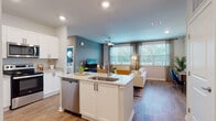 This single-floor residence is designed with a contemporary open-concept layout that seamlessly connects the kitchen and living areas. The kitchen is well-appointed with white shaker-style cabinetry, granite countertops, stainless steel appliances including a refrigerator, dishwasher, microwave, and range, and a central island with a built-in sink. Wood-style flooring runs consistently throughout the unit, contributing to a cohesive and modern aesthetic.

The living room is bright and spacious, featuring oversized windows that allow generous natural light and outdoor views of surrounding greenery. A ceiling fan overhead adds both function and style, while a teal accent wall adds a bold visual element to the space.

The unit includes two bedrooms, each with large windows dressed in sheer curtains and blinds. One bedroom features a teal accent wall, while the other offers a softer, neutral palette. Both provide a calm and comfortable retreat.

Two full bathrooms mirror each other in design, each offering white vanity cabinetry with granite countertops, large mirrors, and a tiled tub-shower combination with wood-style flooring. A generously sized walk-in closet with built-in wire shelving and multi-level hanging rods provides ample storage.