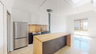 This 1-bedroom, 1-bathroom unit in Memphis, TN offers a thoughtfully designed industrial-modern aesthetic that blends raw architectural character with contemporary upgrades. The open-concept living and kitchen area is anchored by polished concrete floors and soaring ceilings that create a spacious, loft-like atmosphere. A prominent exposed structural column adds an industrial touch, complementing the clean white walls and exposed ductwork overhead. The kitchen is a standout feature, equipped with stainless steel appliances, dark cabinetry, a warm wood-toned backsplash, and a generous butcher block island that doubles as a dining and prep surface. A sleek linear pendant light runs above the island, adding modern polish. Natural light filters in through a window near the living area, enhancing the open feel. The bedroom is bright and airy, featuring the same polished concrete flooring and access to a spacious walk-in closet with built-in shelving. The full bathroom is clean and modern, showcasing a frameless sliding glass shower with white subway tile, a floating vanity with a white countertop, and consistent concrete flooring that ties the unit together cohesively.