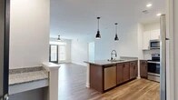 Located in Winston-Salem, NC, this well-appointed 2-bedroom, 2-bathroom single-floor home offers a thoughtfully designed open-concept layout. The combined kitchen and living area serves as the heart of the home, where warm wood-look flooring flows seamlessly throughout. The kitchen is a standout feature, showcasing rich dark lower cabinetry paired with crisp white upper cabinets, a classic subway tile backsplash, granite countertops, and a full suite of stainless steel appliances. A central island with pendant lighting provides additional prep space and a natural gathering point that opens directly into the living area. The living room is bright and welcoming, featuring a glass-paneled entry door with sidelights that invite natural light and outdoor views. The spacious primary bedroom offers plush carpeting, generous closet space, and windows overlooking the surrounding greenery. The second bedroom is equally comfortable, with soft carpet and ample natural light. Both bathrooms are cleanly finished with wood-look flooring and granite vanities. A dedicated laundry room and connecting hallway round out the functional floor plan, making this home as practical as it is comfortable.