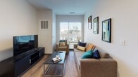 Located at 231 E Washington St in Sandusky, Ohio, this single-floor unit offers a clean, contemporary design with a practical and well-organized layout. The living area is bright and inviting, featuring wood-style flooring, neutral walls, and a large window with blinds that allows natural light to fill the space while offering outdoor views. The room comfortably accommodates seating and entertainment furniture, creating a relaxed yet functional atmosphere.

The kitchen is efficiently designed with sleek grey cabinetry, stainless steel appliances including a refrigerator, microwave, and dishwasher, and a white countertop with an integrated sink. A dining area adjacent to the kitchen provides space for casual meals.

The bedrooms are modestly sized yet functional, each featuring wood-style flooring, large windows for natural light, and sufficient space for a bed and a dedicated study desk with a chair, making them well-suited for both rest and productivity.

The bathroom is finished with a clean, modern aesthetic, including a white vanity with an undermount sink, a large mirror, and a glass-enclosed walk-in shower clad in grey wood-look tile. Wood-style flooring ties the space together cohesively throughout the unit.