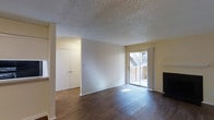 This single-floor residence in Grapevine, Texas offers a clean, functional layout with notable interior details throughout. The main living area showcases dark hardwood flooring that contrasts nicely with the light-toned walls, creating a warm yet bright atmosphere. A textured popcorn ceiling adds a classic touch overhead. Natural light flows into the space through a sliding glass door that opens to an outdoor patio area, providing a convenient indoor-outdoor connection with views of the surrounding exterior. A fireplace anchors one side of the living space, serving as a focal point and adding character to the room. Built-in closet storage with double doors is visible from the main living area, offering practical organization space. The overall layout feels open and well-proportioned, with clean wall surfaces ready for personalization. The combination of natural light, hardwood-style flooring, and the patio access makes this a comfortable and livable space in the heart of Grapevine.