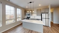 Located at 229 Roberts St N in Fargo, North Dakota, this modern single-floor unit offers a well-designed layout with contemporary finishes throughout. The open-concept kitchen is a standout feature, showcasing gray shaker-style cabinetry, white quartz countertops, a herringbone tile backsplash, and a full suite of stainless steel appliances including an electric range, built-in microwave, dishwasher, and refrigerator. A central island provides additional prep space and anchors the kitchen, while stylish geometric pendant lights add a modern touch overhead. Large windows flood the living area with natural light and frame views of the surrounding Fargo cityscape, complemented by warm wood-look luxury vinyl plank flooring. The bedrooms are carpeted for comfort and each feature generous windows with urban views. Two bathrooms serve the unit: a primary bath with a double-sink vanity featuring gray cabinetry, white quartz counters, marble-look tile flooring, and a walk-in shower, alongside a secondary bath with a single vanity and matching finishes. A dedicated in-unit laundry room with side-by-side washer and dryer and built-in wire shelving adds everyday convenience. The overall aesthetic is clean, neutral, and move-in ready.