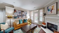 This thoughtfully designed single-floor residence offers a seamless blend of comfort and contemporary style across its well-proportioned living spaces. The living room serves as the heart of the home, showcasing rich hardwood flooring, crisp crown molding, and a fireplace framed by decorative millwork. Natural light streams in through a glass-paneled entry door with transom window, complemented by patterned drapery. Bold abstract artwork and curated décor add a vibrant, artistic character to the space.

Adjacent to the living room, a dedicated dining area features the same warm hardwood flooring and is accented by a large statement painting and a full-wall mirror that enhances the sense of space. The kitchen is equipped with stainless steel appliances, including a refrigerator, range, and over-the-range microwave, set against crisp white cabinetry and granite-look countertops over clean white tile flooring.

The bedrooms are carpeted and bathed in natural light through large windows with sheer drapery, offering a serene retreat. The bathroom features white tile flooring, a tub-shower combination with glass enclosure, white cabinetry with ample vanity space, and recessed lighting throughout. Crown molding is a consistent architectural detail carried across all rooms, lending the residence a polished, refined character.