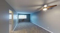 Located at 4225 South Ave in Silverton, Ohio, this single-floor unit offers a practical and comfortable layout across several well-defined living spaces. The main living area is generously sized, finished with plush gray carpeting and painted in a cool blue-gray tone that lends a calm, neutral atmosphere. A ceiling fan with integrated lighting provides both air circulation and overhead illumination, while a window unit ensures climate control. Natural light filters in through windows, brightening the open feel of the room. An adjacent bedroom continues the carpeted flooring and neutral gray wall palette, featuring its own ceiling fan and a window with blinds overlooking the outdoors. A reach-in closet with open shelving provides convenient storage. The kitchen is outfitted with warm wood-toned cabinetry, light countertops, and durable hardwood-style flooring. White appliances, including a gas range and refrigerator, along with a sink, are neatly arranged along one wall, making efficient use of the space. The bathroom is clean and functional, featuring white square wall tiles surrounding a full bathtub and shower combination, a vanity with a framed mirror, and gray-painted walls that complement the overall color scheme throughout the home.