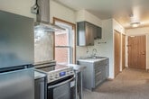 Located at 605 Chase Blvd in Sun Prairie, Wisconsin, this one-bedroom, one-bathroom unit offers a practical and well-organized single-floor layout. The spacious primary bedroom serves as the heart of the unit, accommodating both sleeping and living areas within a generous, open footprint. Soft carpeting, neutral walls, and a large window with blinds allow natural light to fill the room while providing a calm, comfortable ambiance. A compact kitchenette is integrated into the bedroom space, featuring stainless steel appliances including a refrigerator, range with overhead ventilation hood, and gray cabinetry with a countertop workspace — a functional setup ideal for everyday living. The entry area connects to a dedicated closet outfitted with a hanging rod and shelving, providing ample storage, alongside warm wood-toned cabinetry and doors throughout. The bathroom is designed with accessibility in mind, featuring grab bars, a roll-in style shower with a curtain, tile flooring, and clean, minimal finishes. The overall design emphasizes functionality and ease of use, making this unit a practical and comfortable living space in Sun Prairie.