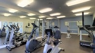 Located at 2979 Green Arbor Ln in Dublin, Ohio, this fitness center offers a well-equipped, single-floor exercise facility designed to support a variety of workout routines. The space is finished with a durable dark floor and painted in cool blue-gray tones, creating a focused and energizing atmosphere. Bright flush-mounted ceiling lights illuminate the room evenly, ensuring excellent visibility throughout the space. Large wall-mounted mirrors line one side of the room, visually expanding the area and allowing users to monitor their form during workouts. The equipment layout is thoughtfully organized, featuring cardio machines including stationary bikes, ellipticals, and treadmills, as well as a multi-station cable and weight machine for strength training. Additional resistance and stretching equipment is positioned along the walls, maximizing the use of available floor space. A wall clock keeps users on schedule, while informational postings near the entrance provide guidance and facility details. The overall design is clean, functional, and purpose-driven, making this fitness center a practical and well-maintained amenity for residents and users of the community.