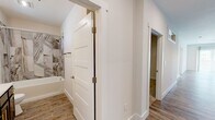 Located at 219 Philema Rd. in Albany, GA, this well-appointed single-story home offers 2 bedrooms and 2 bathrooms with a thoughtfully designed layout. The open-concept kitchen and living area serves as the heart of the home, featuring sleek gray shaker cabinets with gold hardware, quartz countertops, a center island, white subway tile backsplash, and a full suite of stainless steel appliances. Globe pendant lighting adds a modern touch overhead. The living room is bright and airy, with wood-look luxury vinyl flooring, a ceiling fan, and large sliding glass doors that flood the space with natural light and provide access to the outdoors. Both bedrooms are carpeted and comfortably sized, each with a dedicated closet. The primary bedroom features a generous walk-in closet with built-in shelving. The two bathrooms are finished with quartz countertops and striking marble-look tile surrounds on the tub-shower combos. One bathroom showcases navy-blue cabinetry with gold accents and a large mirror, while the second offers a clean, neutral aesthetic with a built-in shower niche. A utility room and two closets round out the functional layout of this move-in ready home.