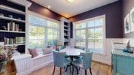 Located at 380 Mather St in Hamden, Connecticut, this thoughtfully designed dining room offers a distinctive blend of classic architectural details and coastal-inspired style. The room is finished with crisp white beadboard wainscoting along the lower walls, which transitions to rich purple-toned upper walls, creating a bold yet elegant two-tone effect. Light hardwood flooring runs throughout, adding warmth and continuity to the space. A large picture window flanked by white plantation shutters floods the room with natural light and offers views of the surrounding greenery. Built-in shelving units frame the window and a cozy window bench seat, providing both functional storage and an inviting nook. A round marble-top dining table is centered in the room, surrounded by tufted light blue leather chairs with nailhead trim, lending a refined, sophisticated touch. A distressed turquoise sideboard adds a pop of color and serves as a functional accent piece. Botanical art prints adorn the walls, complementing the coastal aesthetic. A gold-framed console table with a glass shelf and fresh floral arrangement adds an elegant finishing touch. The room is accessed through a glass-paned interior door, enhancing its open and airy feel.