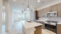 Located in Austin, TX, this modern 1-bedroom, 1-bathroom residence offers a thoughtfully designed open-concept floor plan that maximizes every square foot. Light wood-style flooring flows seamlessly throughout, creating a cohesive and airy aesthetic.

The combined kitchen and living area serves as the heart of the home. The kitchen is a standout feature, anchored by a large center island with a striking white quartz waterfall countertop and an undermount sink with a professional-style faucet. Pendant globe lights hang above the island, adding warmth and style. Cabinetry in a warm wood-grain finish lines the walls, complemented by a classic subway tile backsplash and stainless steel appliances including a gas range, built-in microwave, and French door refrigerator. The living area extends naturally from the kitchen, with access to a private patio door and large windows that invite abundant natural light and outdoor views.

The bedroom is a comfortable retreat with generous proportions, a ceiling fan, and wide windows overlooking greenery. A dedicated walk-in closet features wrap-around shelving and hanging rods for ample storage.

The bathroom is elegantly appointed with a dual-sink vanity topped in white quartz, warm wood cabinetry with matte black hardware, a large mirror with modern light bar, and a glass-enclosed walk-in shower with a rain showerhead and tile surround.