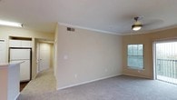 Located at 8585 Spicewood Springs Rd in Austin, Texas, this single-story space offers a clean and functional layout with a warm, neutral aesthetic throughout. The main living area is finished with wall-to-wall carpeting that adds a sense of comfort underfoot, while crown molding along the ceiling lends a refined, classic touch to the interior. A ceiling fan provides year-round climate comfort, and a window allows natural light to filter into the space, brightening the room with an open, airy feel. The walls are painted in a soft, warm beige tone, contributing to a welcoming and cohesive atmosphere. A hallway visible from the main area connects to additional rooms, each accessible via paneled doors that maintain a consistent, understated design language. HVAC vents are integrated into the ceiling, ensuring efficient climate control throughout. The overall layout is straightforward and versatile, offering a practical living environment well-suited for a variety of uses. The single-floor design ensures ease of accessibility and a seamless flow between spaces.
